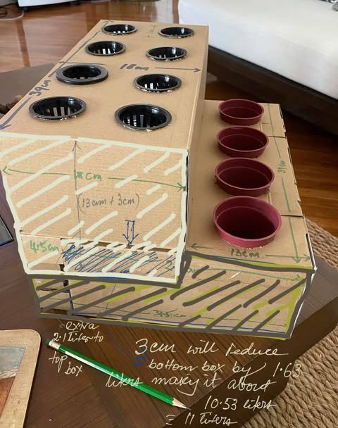 A cardboard mock-up of a two-tier growing unit, marked up by hand with dimensions and reservoir volumes